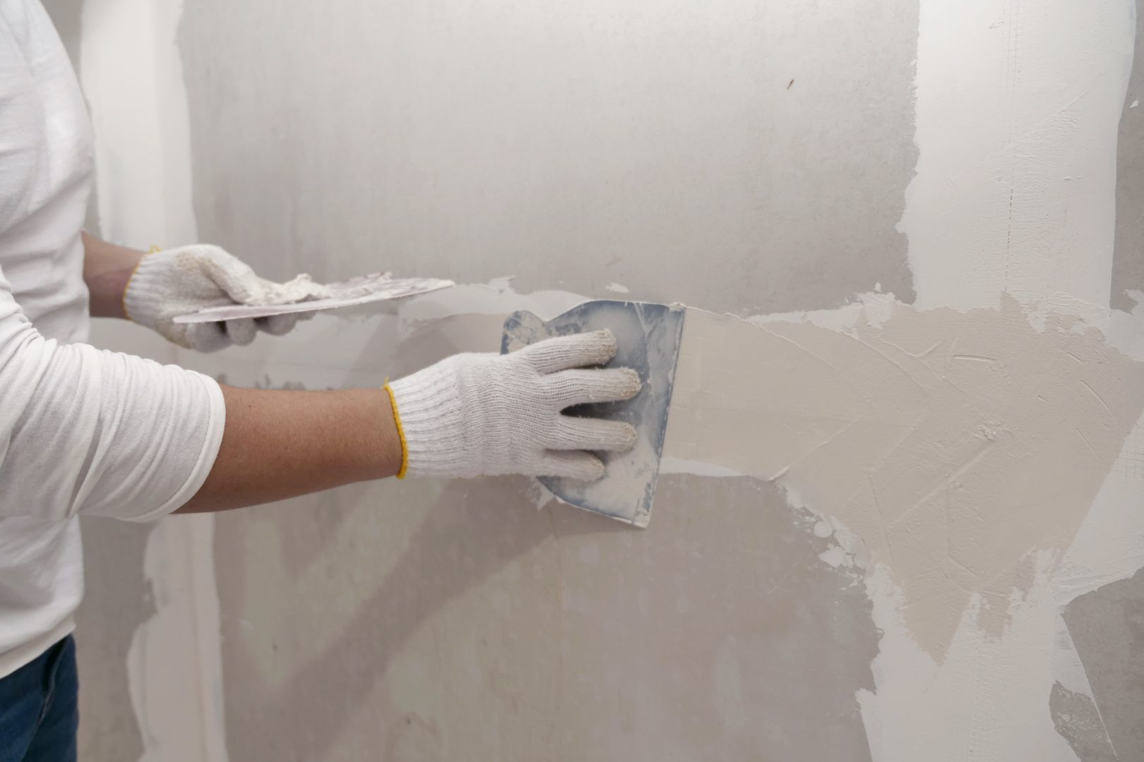Plasterwork And Wall Painting Preparation. Asian Male Applying Filling Drywall Patch.